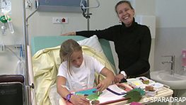 Après la pose d'un cathéter court qui a été difficile, une petite fille fait de la peinture dans sa chambre en hôpital de jour, sa maman à côté d'elle.