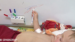 Un petit garçon fait des gribouillages sur un tableau effaçable à sec disposé juste à côté de la table d'examen pendant une prise de sang.