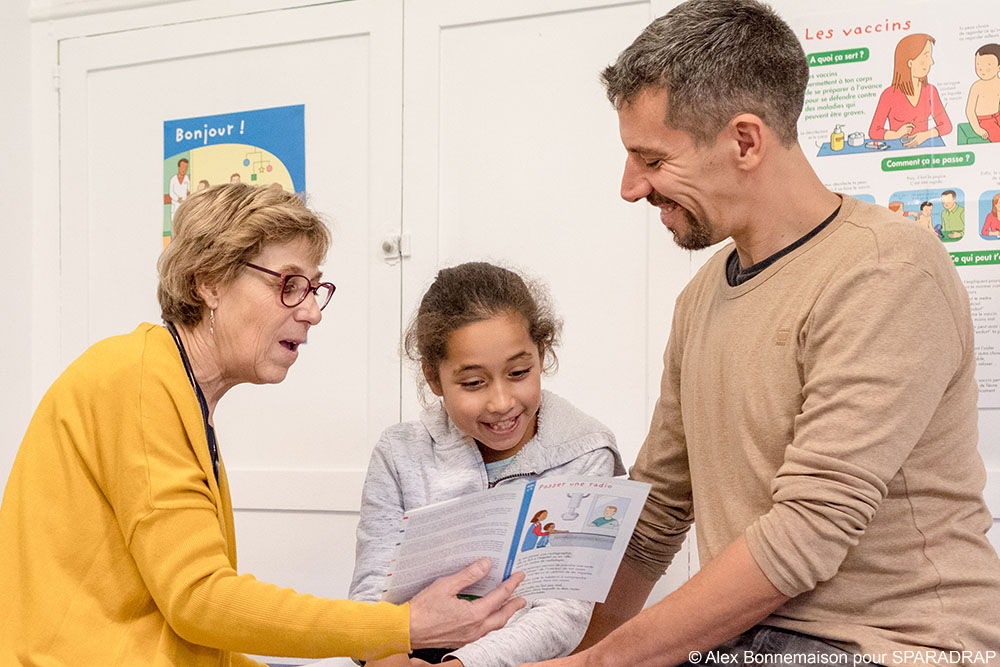Un papa auprès de sa fille alors qu'une médecin lui montre une fiche SPARADRAP