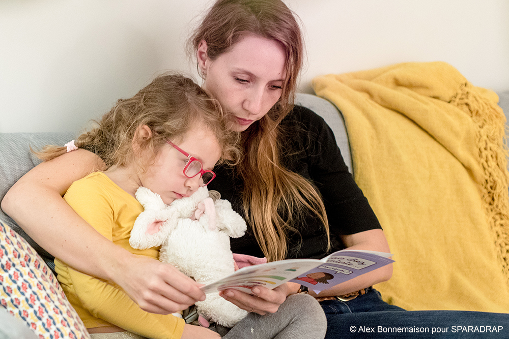 Une maman lit un guide SPARADRAP avec sa fille et son doudou